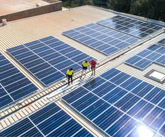 Three solar experts on a rooftop, overseeing solar panels generating clean energy on a building.